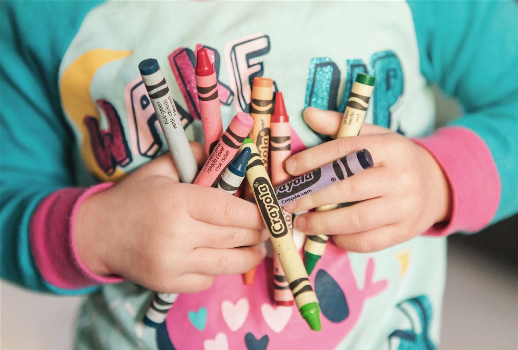  child in a teal shirt holding two hands full of crayons