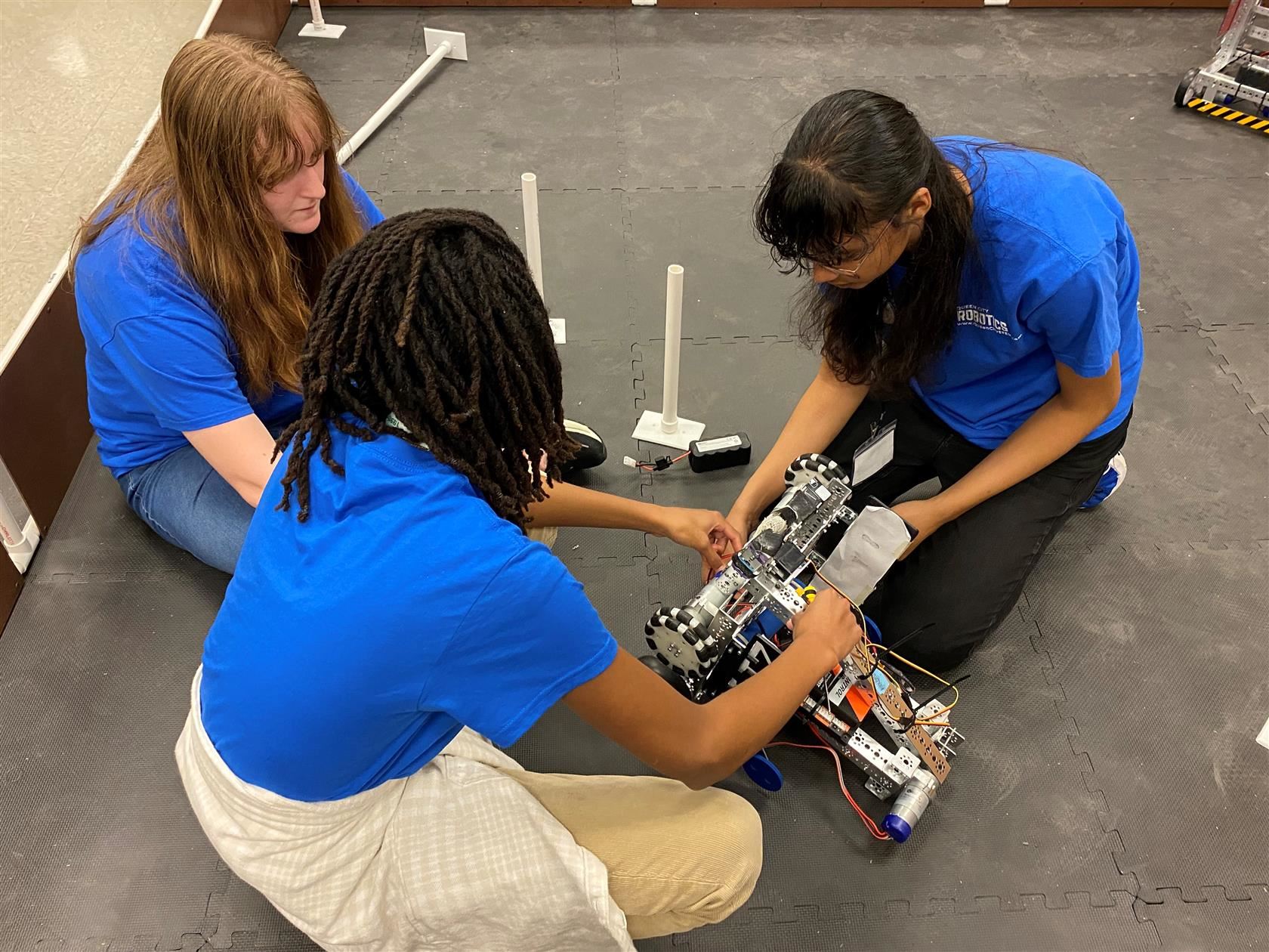  Students in blue shirts working on a robotics project on the ground