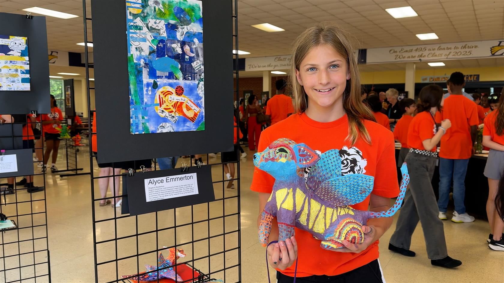  Student stands in front of collage holding sculpture