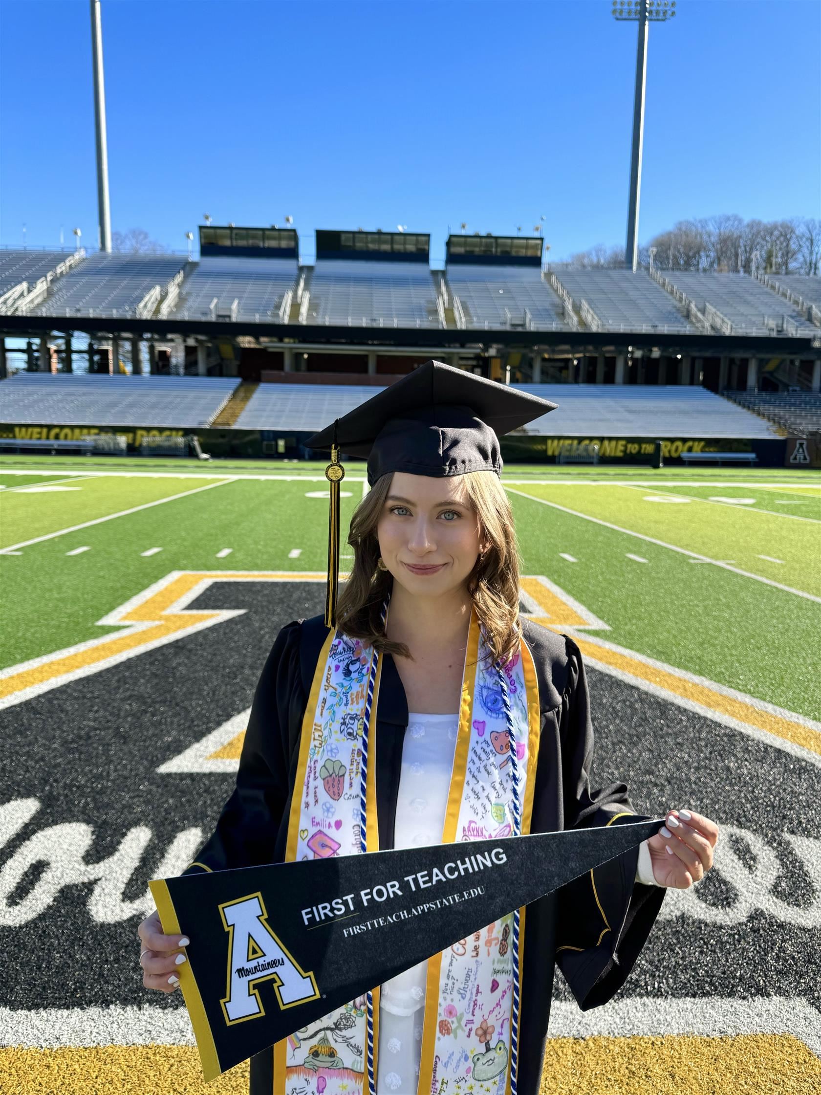 Katherine McDonald wearing her Appalachian State cap and gown and holding a App State flag