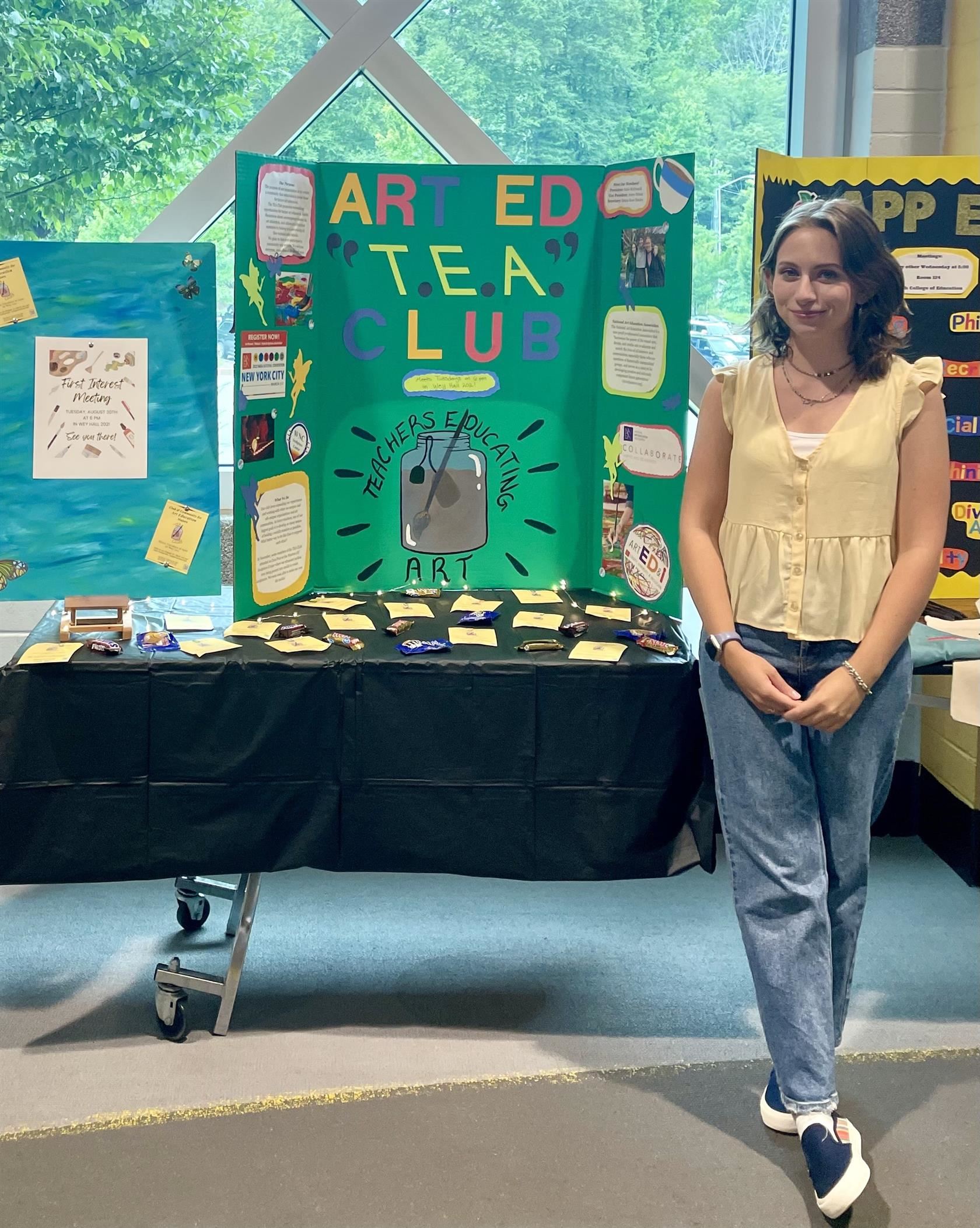 Katherine McDonald standing in front of an "Art Ed T.E.A. Club" poster