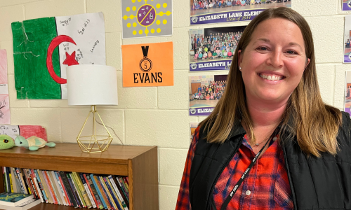  Courtney Evans smiles in front of a bookcase and wall posters and pictures
