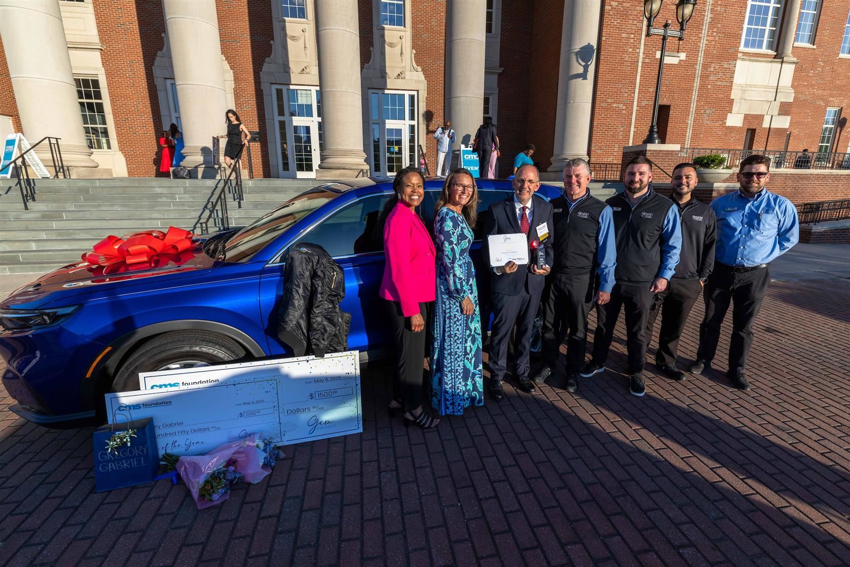 Gregory Gabriel smiles in front of his new car alongside reps from Hendrick Automotive Group and CMS leaders