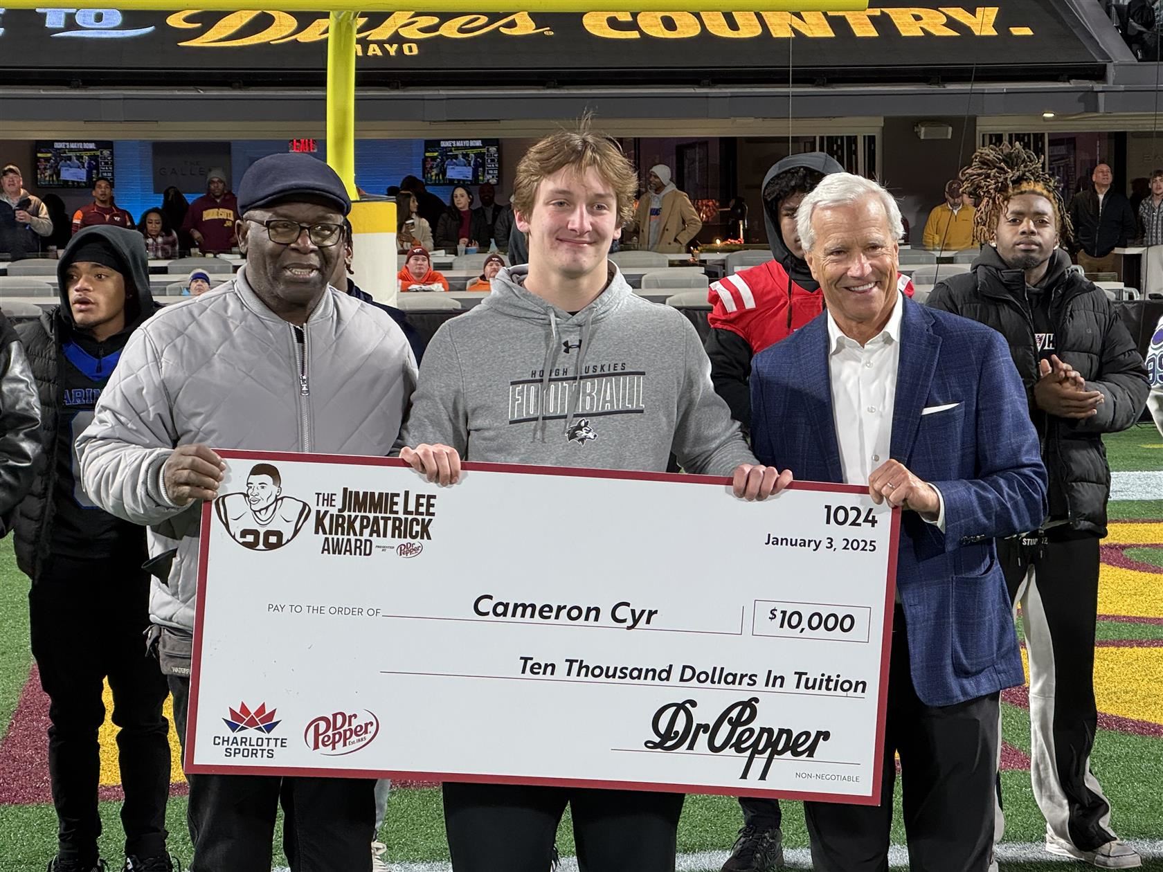 William Amos Hough High senior Cameron Cyr (center) stands and holds a scholarship check.