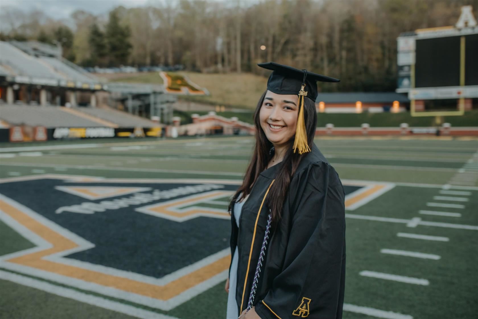 Melissa Castaneda in her cap and gown on the football field at App State.