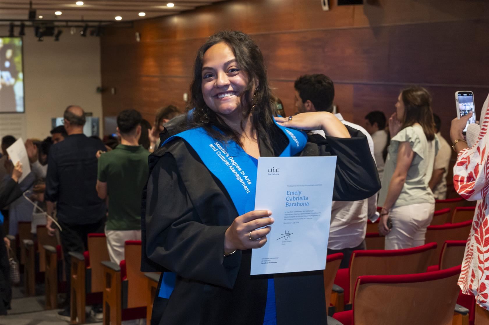 Emely Barahona smiles big with her master's degree from the Universitat Internacional de Catalunya