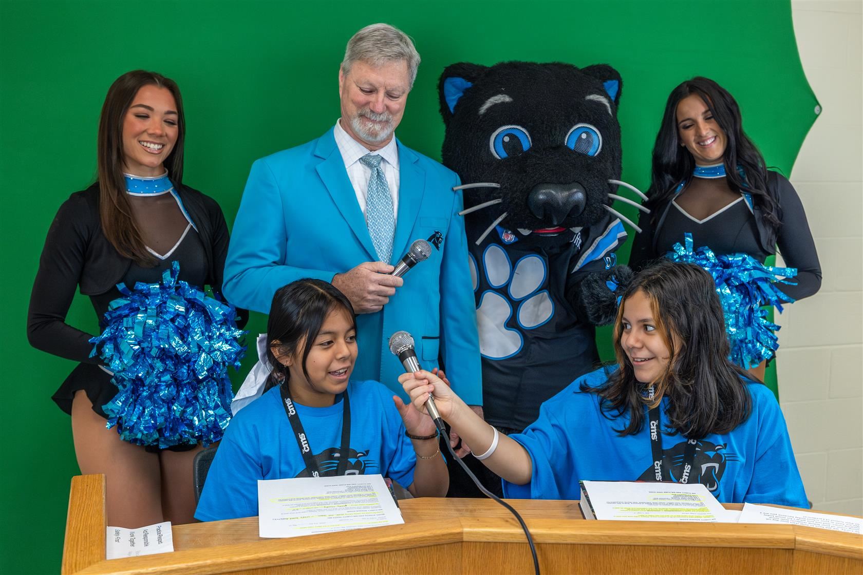 Two MOIA students host the morning announcements with Sir Purr and other Carolina Panthers' staff.