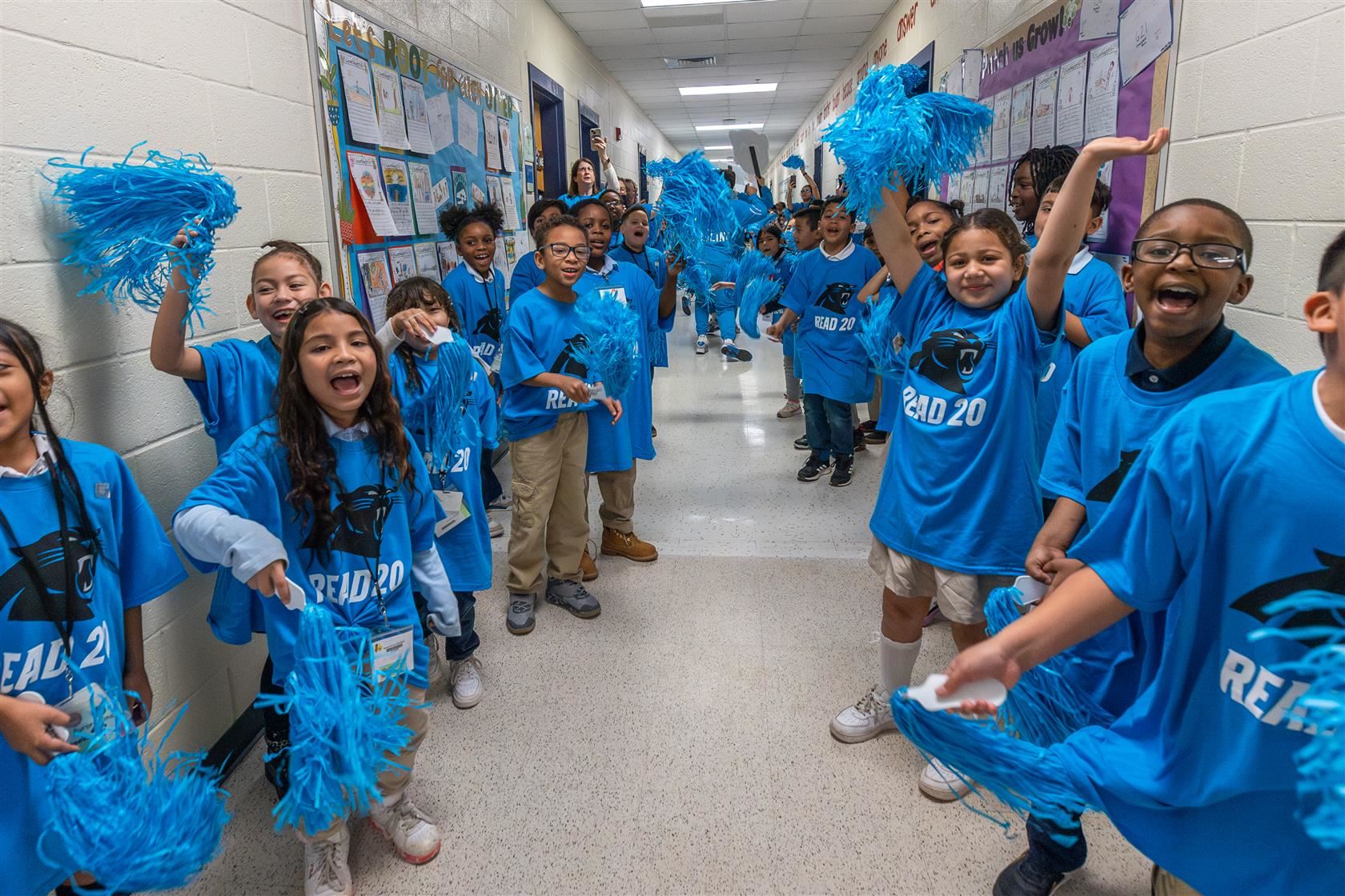 MOIA students line the hall and cheer while wearing Carolina Panthers' t-shirts and waving blue pom poms 