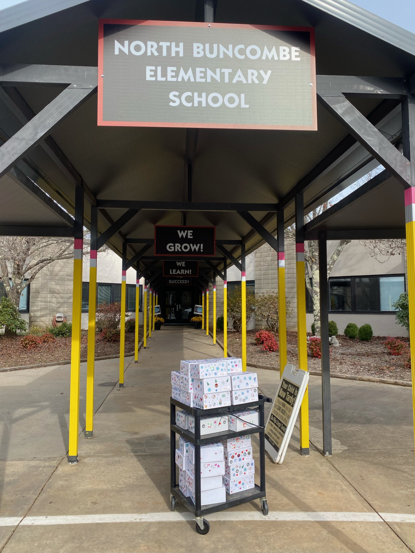 A cart of kindness boxes sits under a sign that reads North Buncombe Elementary School.