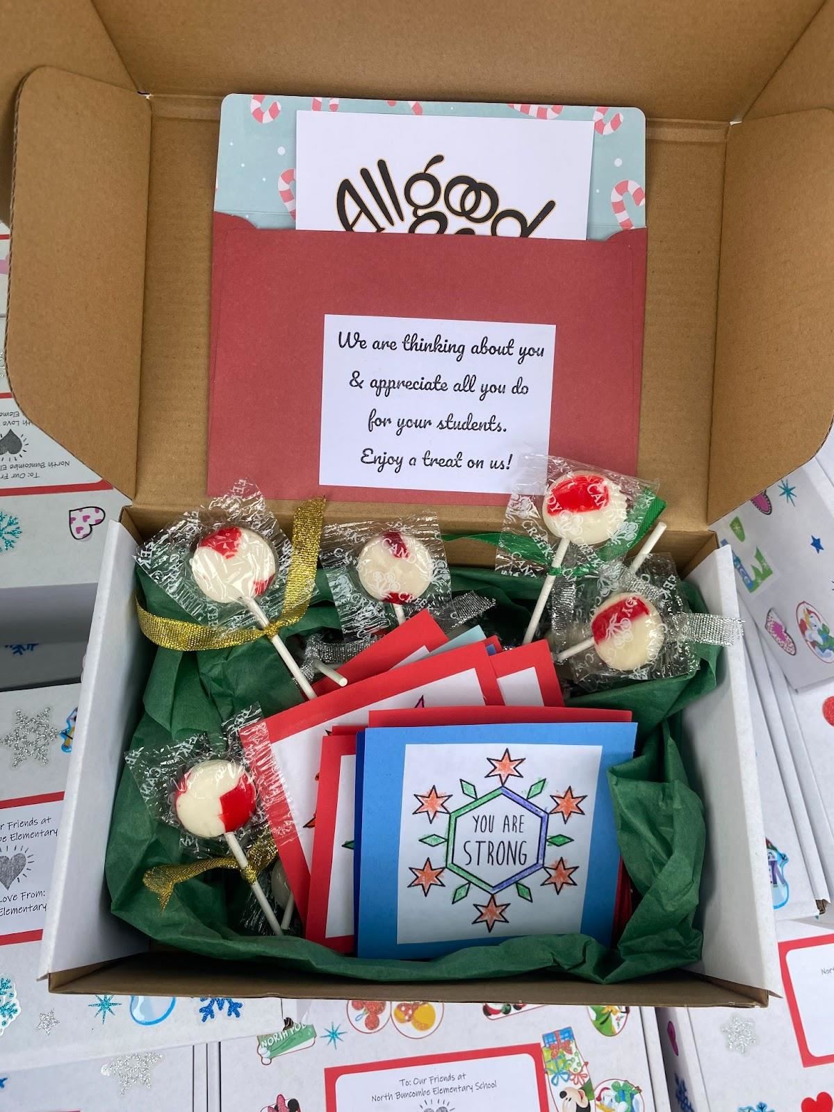 An opened kindness box shows notes of encouragement and lollipops.