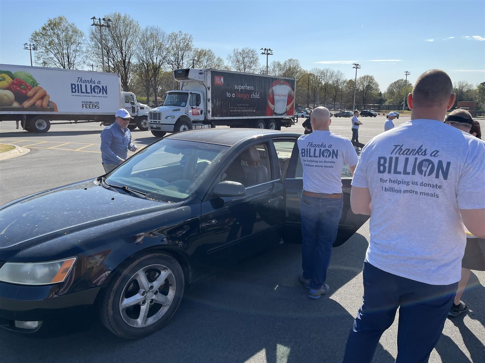Volunteers open a car door to place groceries in the car.