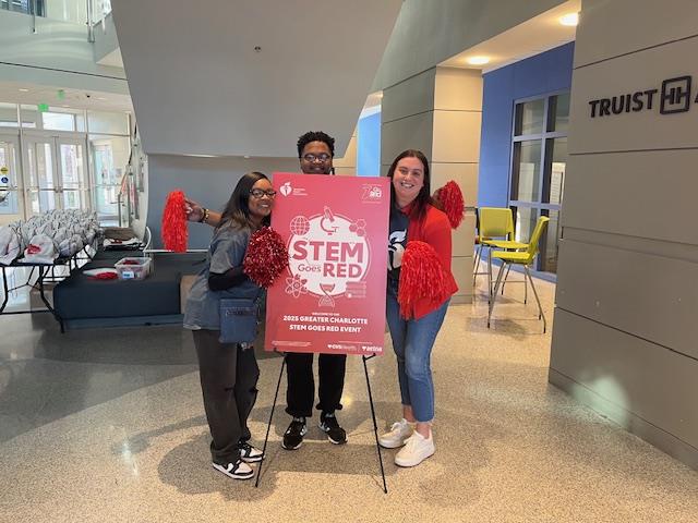 Volunteers stand around a STEM Goes Red Event sign